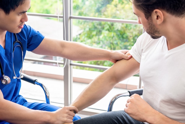 Asiatischer Arzttherapeut massiert schmerzenden Arm des männlichen Athletenpatienten in der Klinik für physikalisches Therapiekonzept