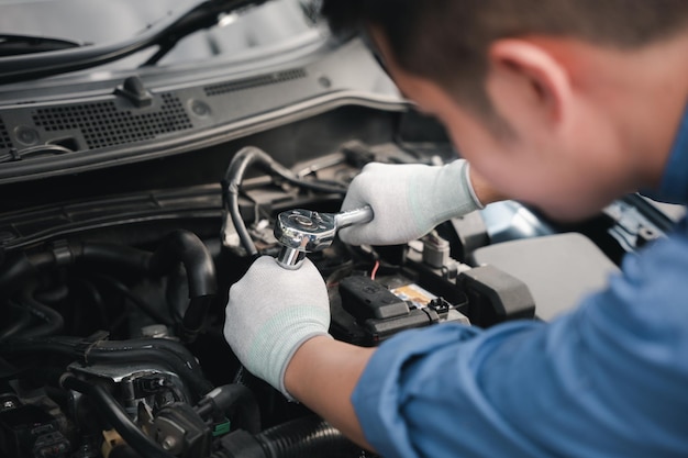 Asiatischer Automechaniker, der mit einem Schlüssel zur Reparatur und Wartung an einem Automotor arbeitet