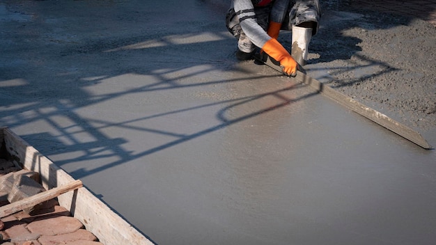 Asiatischer Bauarbeiter, der eine lange dreieckige Kelle verwendet, um den Zementboden auf der Baustelle zu verputzen