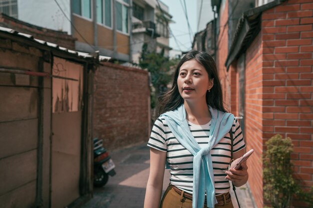 asiatischer besucher, der in der alten straße spaziert. Frau, die ein Telefon hält.