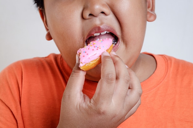 Asiatischer fetter Junge hält einen mit Erdbeeren überzogenen Donut