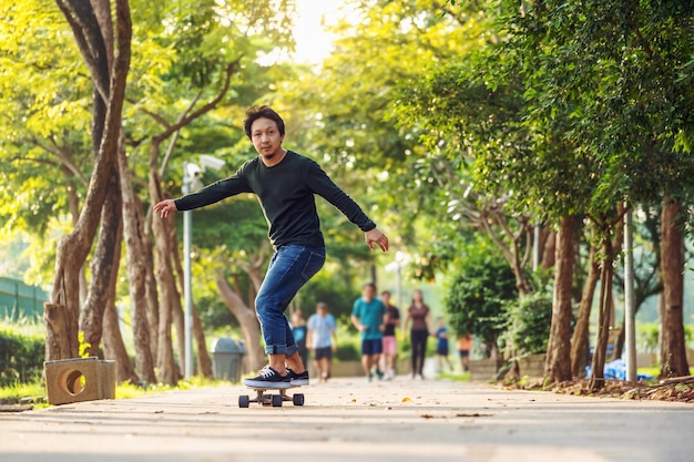 Asiatischer fröhlicher Mann, der Surfskate oder Skateboard im Freiluftpark spielt