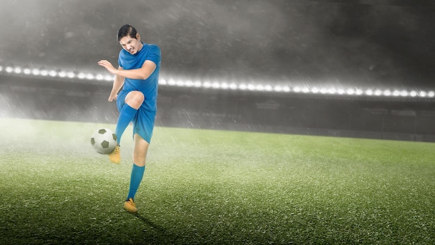 Asiatischer Fußballspielermann in einem blauen Trikot, der den Ball tritt