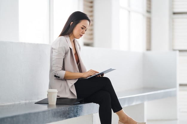 Asiatischer Geschäftsfrauenberuf mit einem digitalen Tablet im Bürokorridor während der Kaffeepause