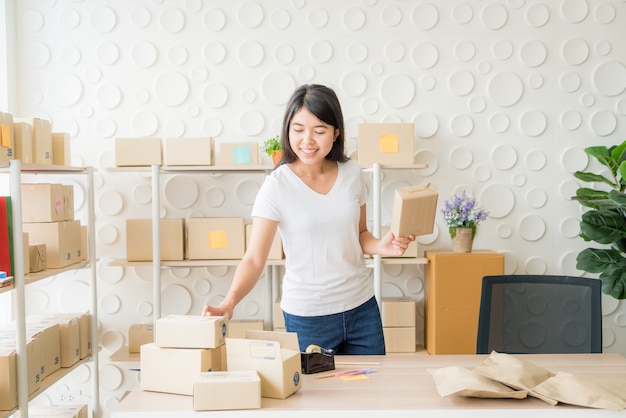 Asiatischer Geschäftsinhaber, der zu Hause mit Packbox am Arbeitsplatz arbeitet