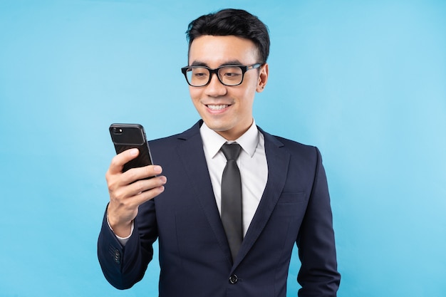Asiatischer Geschäftsmann, der Anzug hält Smartphone an der blauen Wand hält