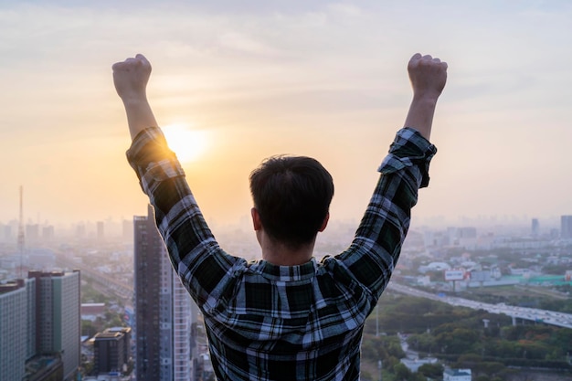 Asiatischer Geschäftsmann, der auf einem hohen Gebäude steht und stolz darauf ist, Erfolg zu haben Sunset background Business Winner Award