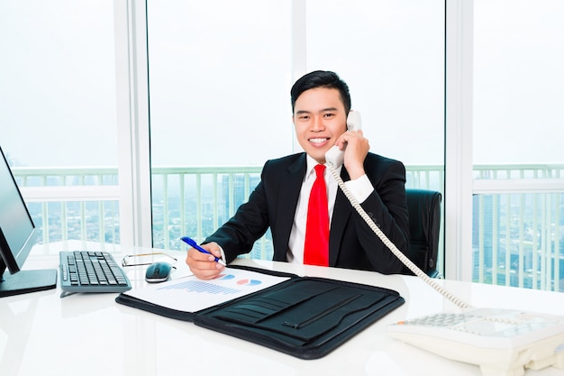 Asiatischer Geschäftsmann, der im Bürokontrollgewinn telefoniert