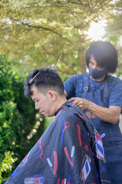 Asiatischer Geschäftsmann, der im Hausgarten Haarschnitt macht. Soziale Distanzierung und neuer normaler Lebensstil.