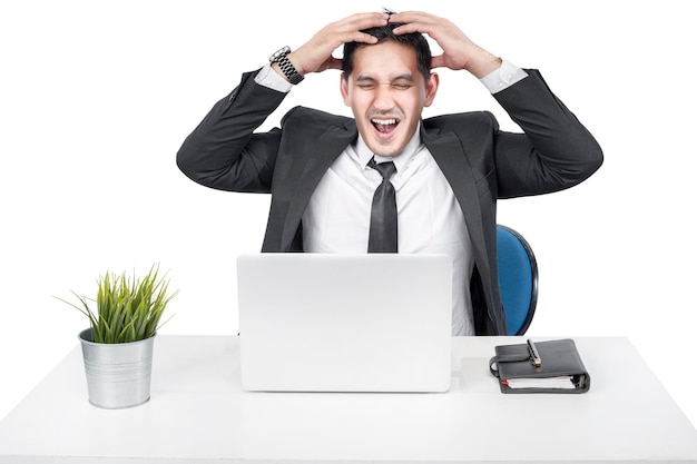 Asiatischer Geschäftsmann, der mit einem gestressten Ausdruck mit einem Laptop auf dem Schreibtisch sitzt