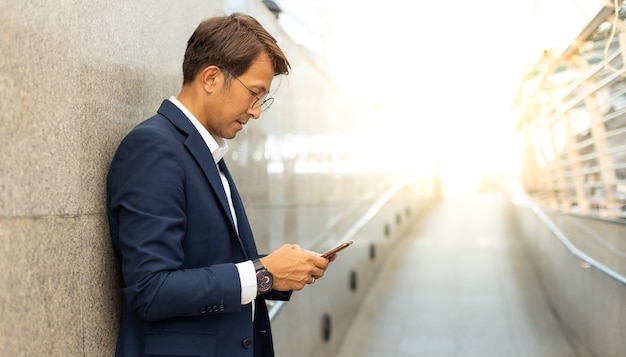 Asiatischer Geschäftsmann mit Handy-App-SMS außerhalb des Bürogebäudes