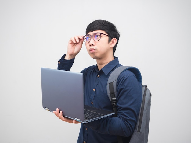 Asiatischer Geschäftsmann mit Rucksack, der einen Laptop hält, der verwirrt ist, seine Brille zu berühren?