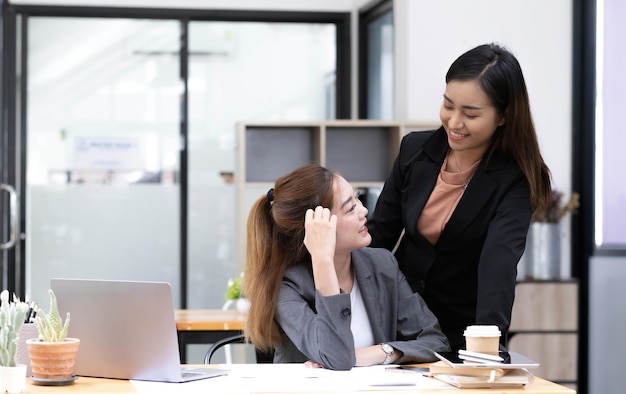 Asiatischer Geschäftsmann präsentiert und erklärt die Arbeit einer Kollegin mit Laptop-Computer nachts im Büro Teamwork-Mitarbeiter-Kooperations-Finanzmarketing-Team oder Unternehmenskonzept