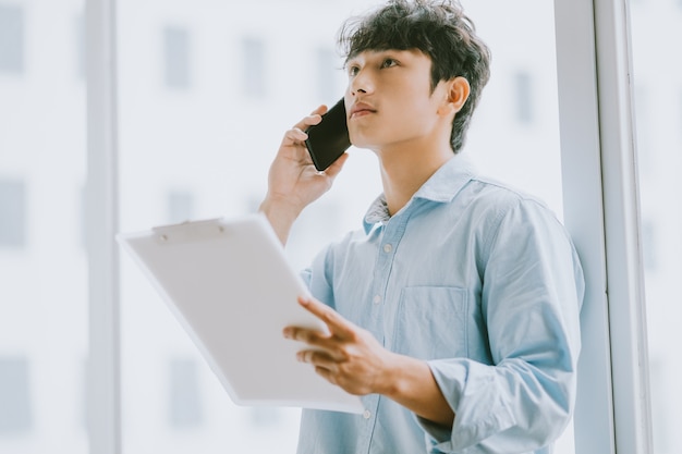 Asiatischer Geschäftsmann ruft an, um über die Arbeit am Fenster zu diskutieren