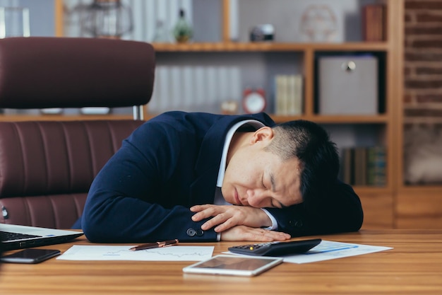 Asiatischer Geschäftsmann schläft müde auf dem Tisch liegend Mann bei der Arbeit