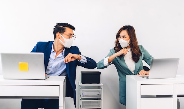 Asiatischer Geschäftsmann und Frau mit Gesichtsmaske und Ellbogen zusammen mit Druckern im Büro