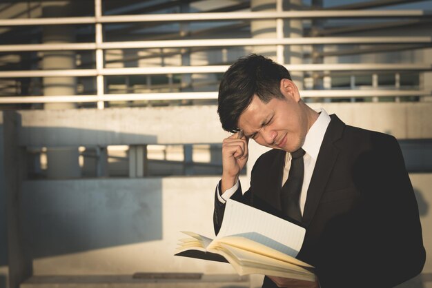 Asiatischer Geschäftsmannstress mit einem Buch im Gebäude