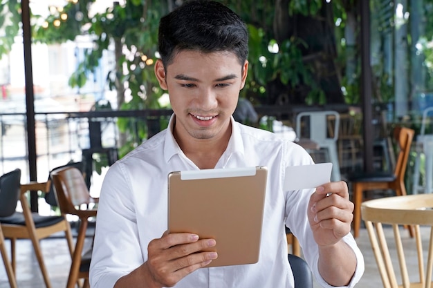 Asiatischer gutaussehender Geschäftsmann oder Büroangestellter oder junger Student, der Kredit- oder Lastschrift verwendet