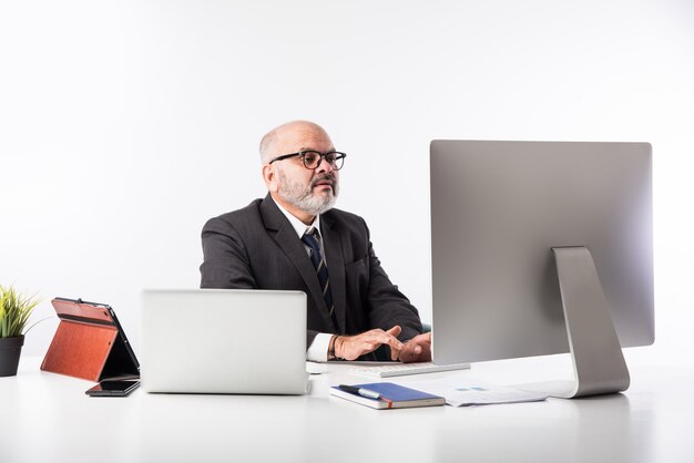 Asiatischer indischer leitender Finanzgeschäftsmann, der an seinem Arbeitsplatz oder Schreibtisch vor einem Computer, Laptop und Tablet sitzt. Telefonieren, während ich Papierkram erledige