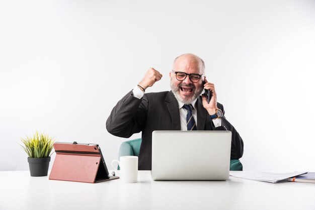 Asiatischer indischer leitender Finanzgeschäftsmann, der an seinem Arbeitsplatz oder Schreibtisch vor einem Computer, Laptop und Tablet sitzt. Telefonieren, während ich Papierkram erledige