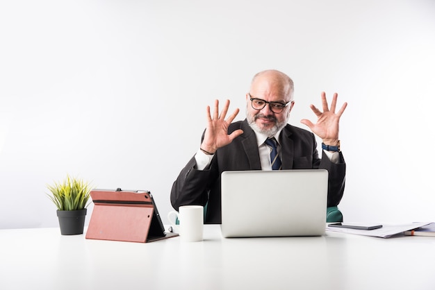 Asiatischer indischer leitender Finanzgeschäftsmann, der an seinem Arbeitsplatz oder Schreibtisch vor einem Computer, Laptop und Tablet sitzt. Telefonieren, während ich Papierkram erledige