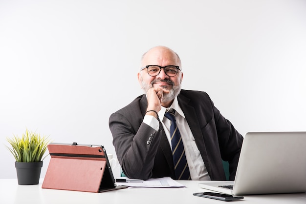 Asiatischer indischer leitender Finanzgeschäftsmann, der an seinem Arbeitsplatz oder Schreibtisch vor einem Computer, Laptop und Tablet sitzt. Telefonieren, während ich Papierkram erledige