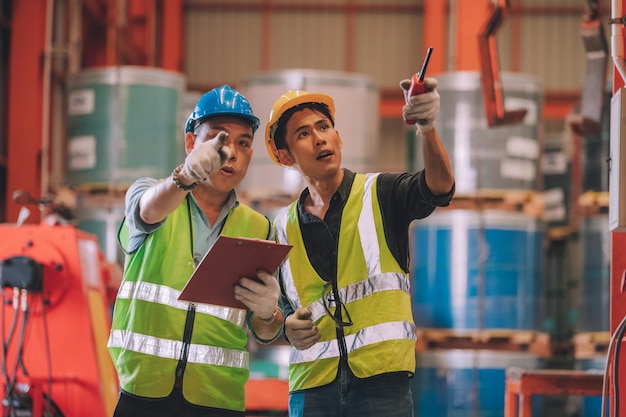 Asiatischer Ingenieur-Fabrikleiter und Mechaniker-Angestellter in Sicherheitshelmgesprächen und -inspektion in der Fabrik