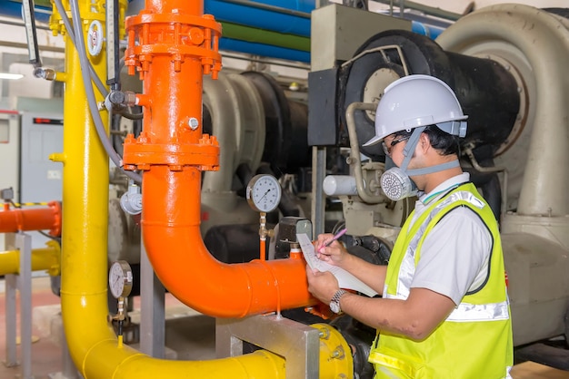 Foto asiatischer ingenieur mit brille, der im heizraum arbeitet und die technischen daten der heizungsanlage überprüft. menschen in thailand, die eine gasmaske tragen