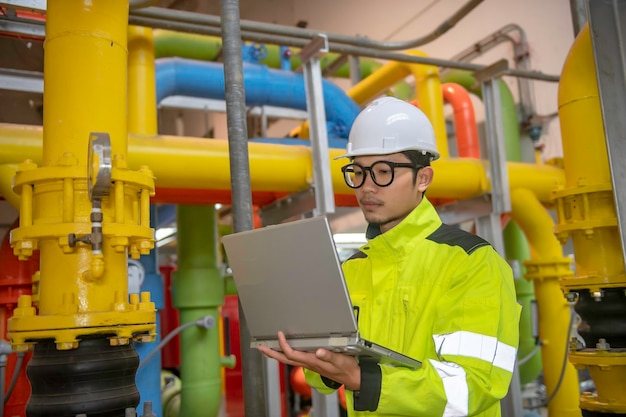 Asiatischer Ingenieur mit Brille, der im Heizraum arbeitet und die technischen Daten der Heizungsanlagen überprüft