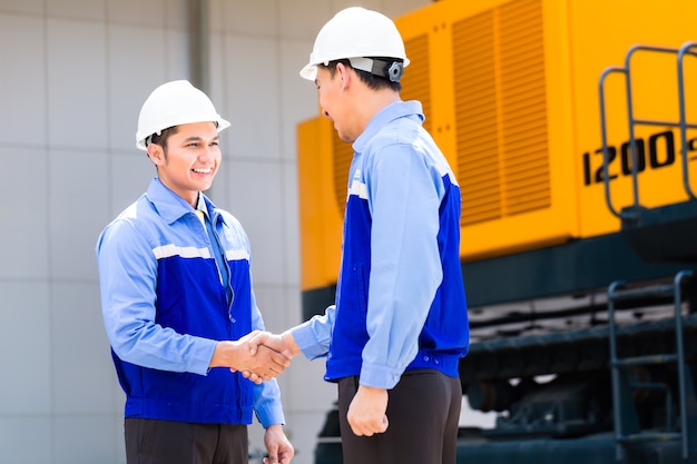 Asiatischer Ingenieur mit Vereinbarung Handschlag an Baumaschinen der Baustelle