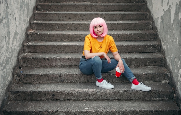 Asiatischer jugendlicher Hipster, der auf Stadtstraße sitzt