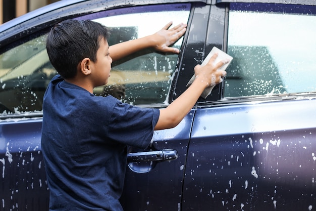 Asiatischer junge, der autofenster mit schwamm und seifenschaum wäscht