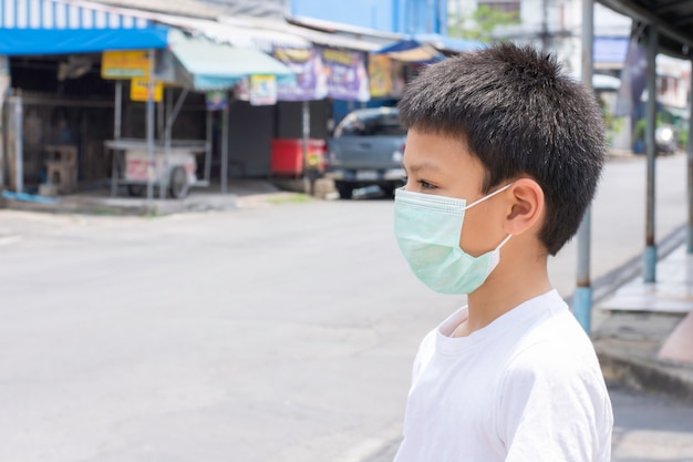 Asiatischer Junge, der eine Maske trägt, die auf der Straße in Bangkok, Thailand steht.