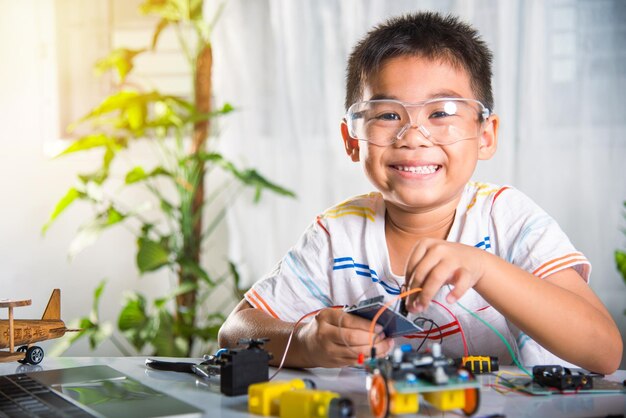 Asiatischer Junge, der Energie- und Signalkabel an Sensorchip mit Arduino-Roboterauto anschließt