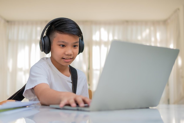 Asiatischer Junge, der Gitarre spielt und Online-Kurse auf dem Laptop anschaut, während er für das Erlernen von Musik übt