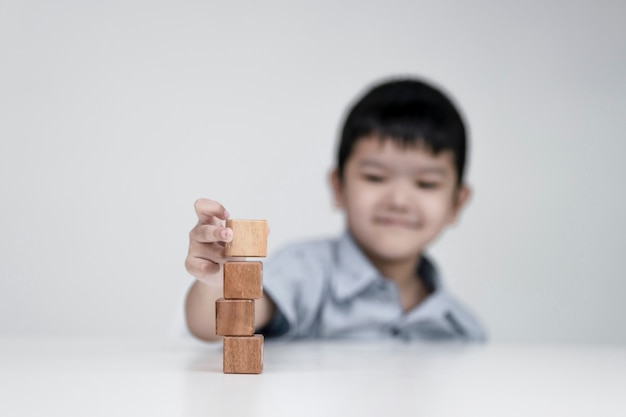 Asiatischer Junge, der Holzwürfel, Bildungskonzepte und das Lernen in einer neuen Normalität wählt.