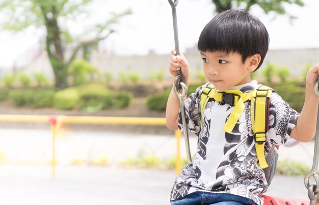 Asiatischer Junge, der im Spielplatz mit hellem Kopienraum schwingt