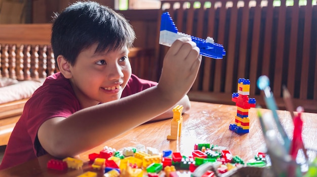 Asiatischer Junge, der kreativ wird, wenn er bunte Plastikziegel-Spielzeugflugzeuge glücklich und lustig zu Hause zusammenbaut