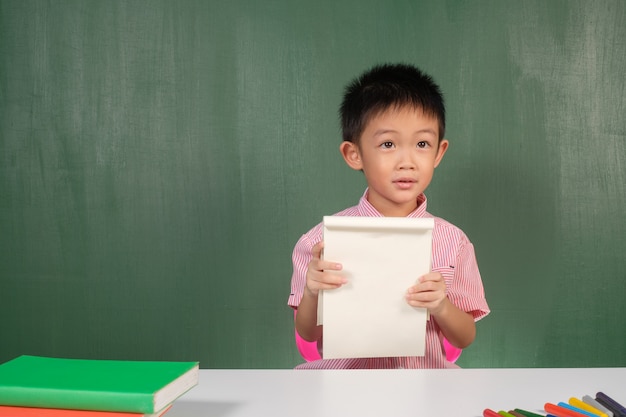 Asiatischer Junge, der leeres Notizbuch im Kreidebrettraum zeigt