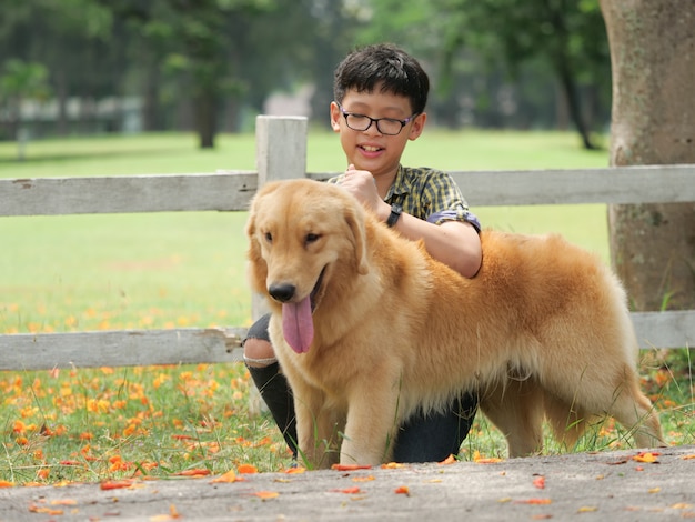 Asiatischer Junge, der mit Hündchen goldenem retreiver im Park spielt