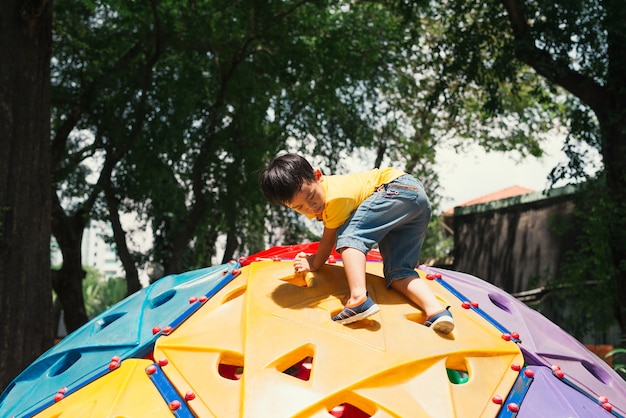 Asiatischer junge, der spaß hat, auf dem kletterspielzeug für kinder auf dem schulhof zu spielen, zurück zu den aktivitäten im freien