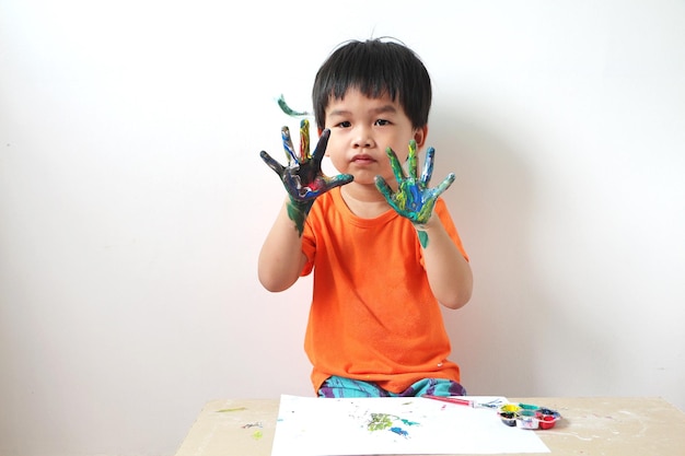 Asiatischer Junge lernt, Aquarelle zu verwenden, indem er auf seine Hände malt Kleines Kind hat Aquarell auf seiner Handfläche gemalt