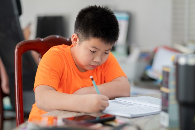 Asiatischer Junge macht Hausaufgaben, Kind schreibt Papier, Bildungskonzept, zurück zur Schule