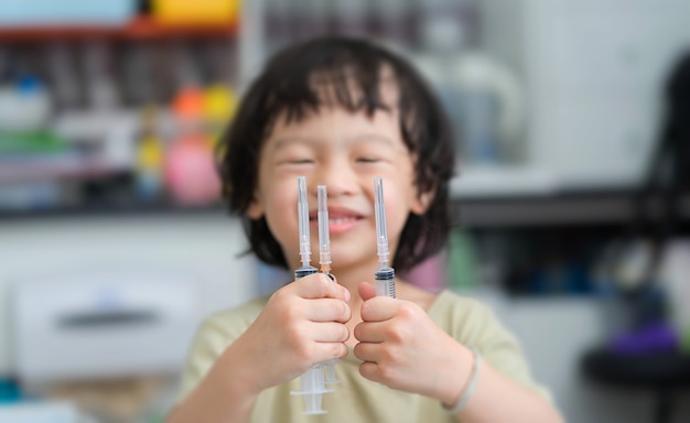 Asiatischer Junge mit dem Lächelngesicht, das an Hand drei Spritzen auf Unschärfehintergrund hält