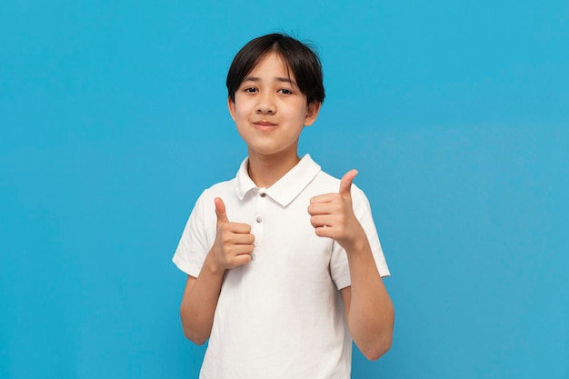 Foto asiatischer junge von zwölf jahren im weißen t-shirt zeigt likes mit seinen händen auf blauem hintergrund