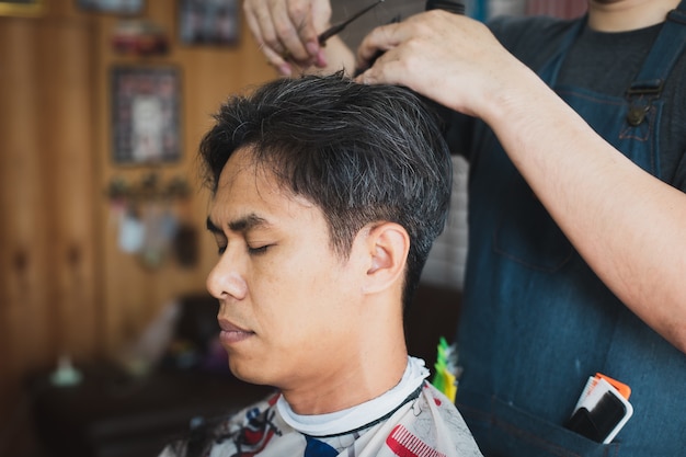 Asiatischer junger Mann, der Haarschnitt mit Schere durch professionellen Friseur im Friseursalon ist. Friseur mit Kamm und Schere schneiden Haare.