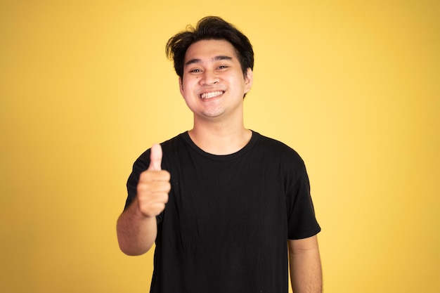 Asiatischer junger Mann, der sich Daumen mit lächelnden Zähnen zeigt