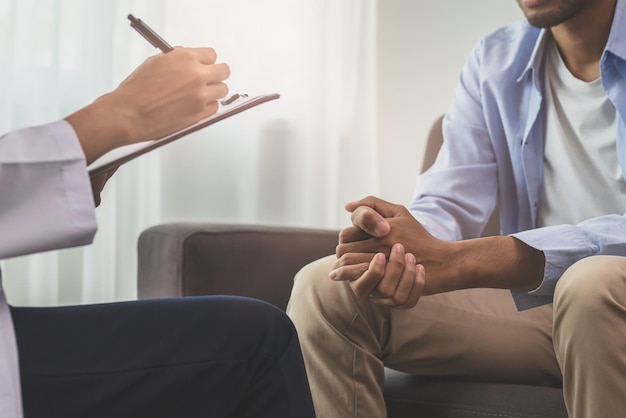 Asiatischer junger Mann, männlich, hat psychische Symptome, die Therapie und Stress gewesen sein müssen, sitzt auf der Couch, um während der Sitzung einen Psychologen zu konsultieren, und macht sich Notizen, um herauszufinden, wie der Therapeut behandelt werden soll.