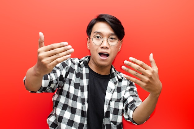 Asiatischer junger Mann mit Brille, der dazu einlädt, mit der Hand einzeln auf rotem Hintergrund zu kommen.