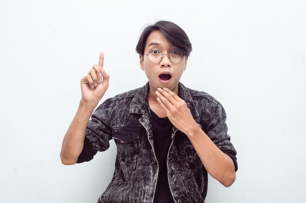 asiatischer junger mann mit brille schockiert, der glücklich mit dem finger zeigt, um platz zu kopieren und etwas waren anzubieten